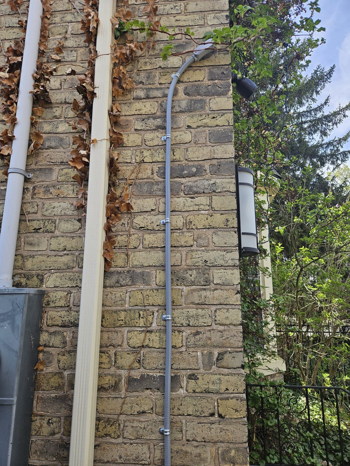 Liquid-tight conduit running down a brick wall to a black UniFi G6 bullet camera