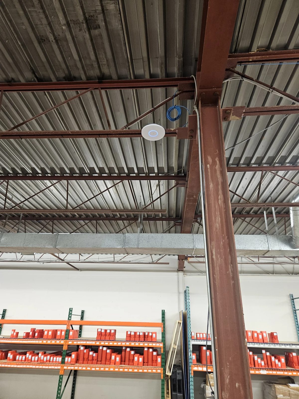 Ceiling-mounted UniFi U7 Pro XG WiFi access point with a service loop installed in a warehouse