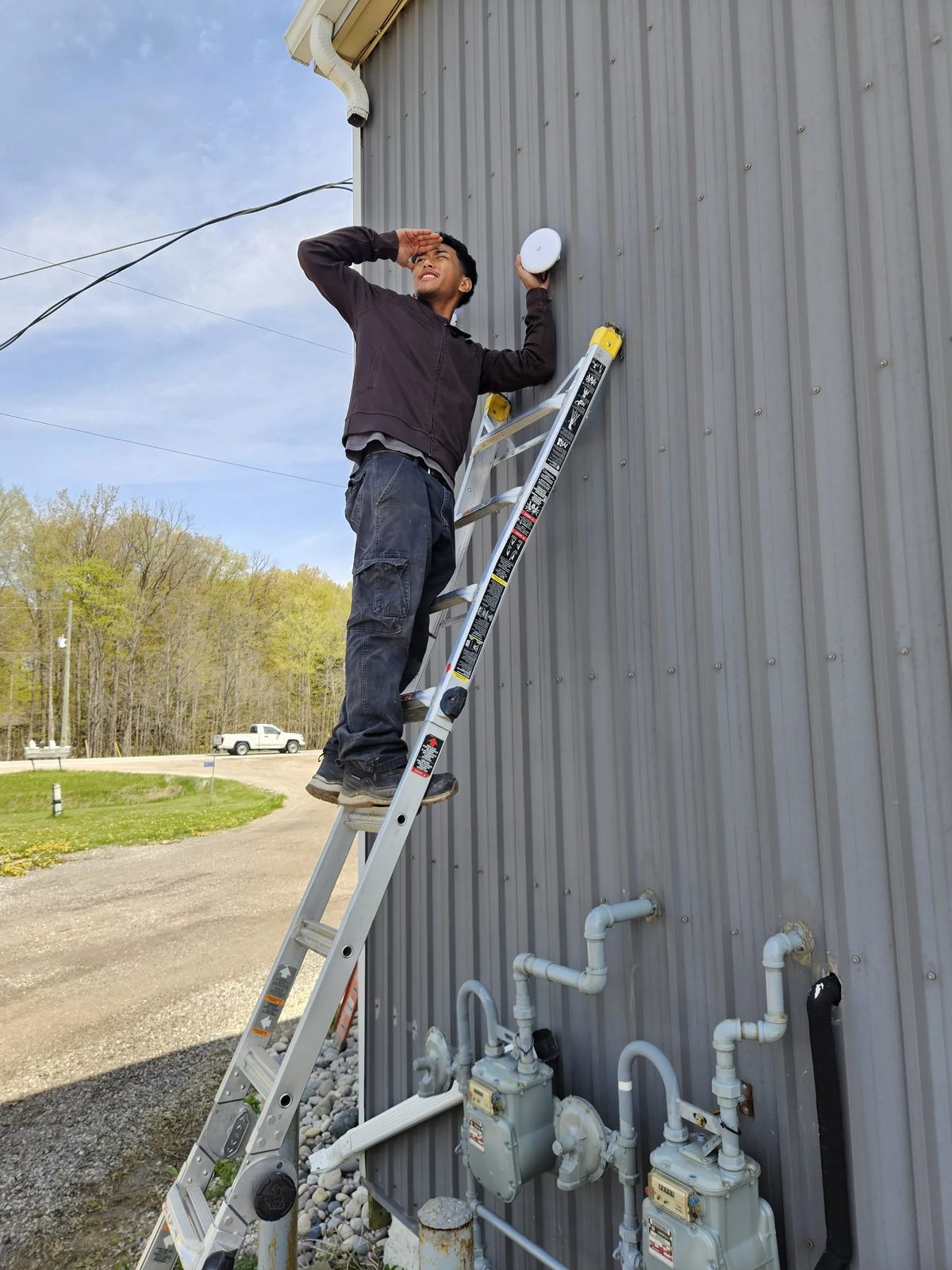 London Tech Solutions technician aiming a UniFi Building Bridge point-to-point radio on a steel building in Ilderton Ontario