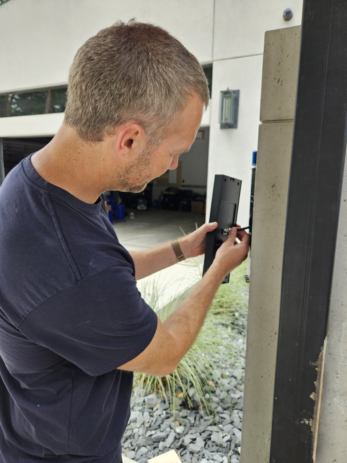 Technician wiring a UniFi G3 Intercom back through a concrete gate pillar to the home network and NVR