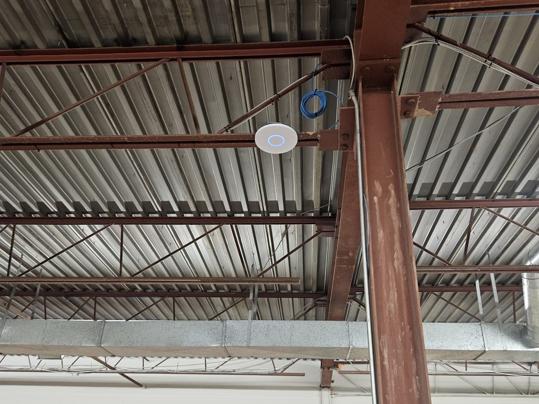 UniFi WiFi access point mounted on the ceiling of a commercial warehouse in London Ontario